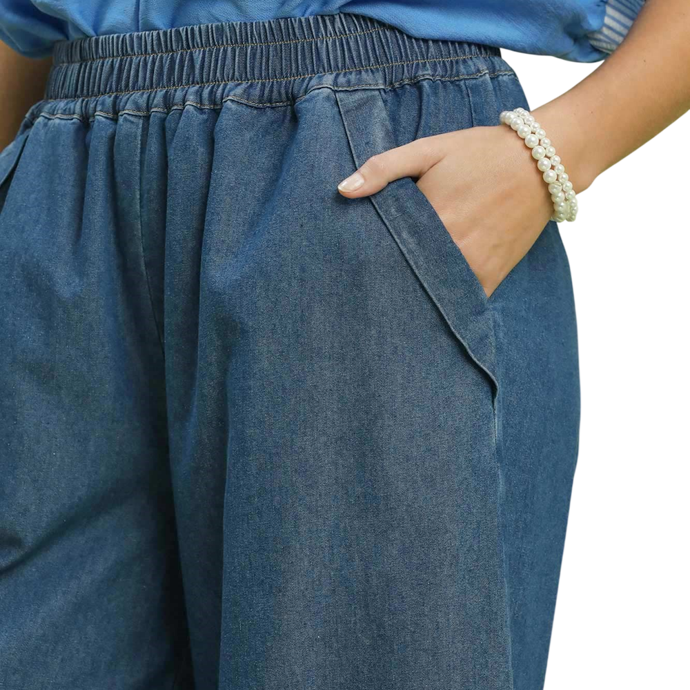 A close-up of a person wearing blue denim chambray pants with an elastic waistband and side pockets.