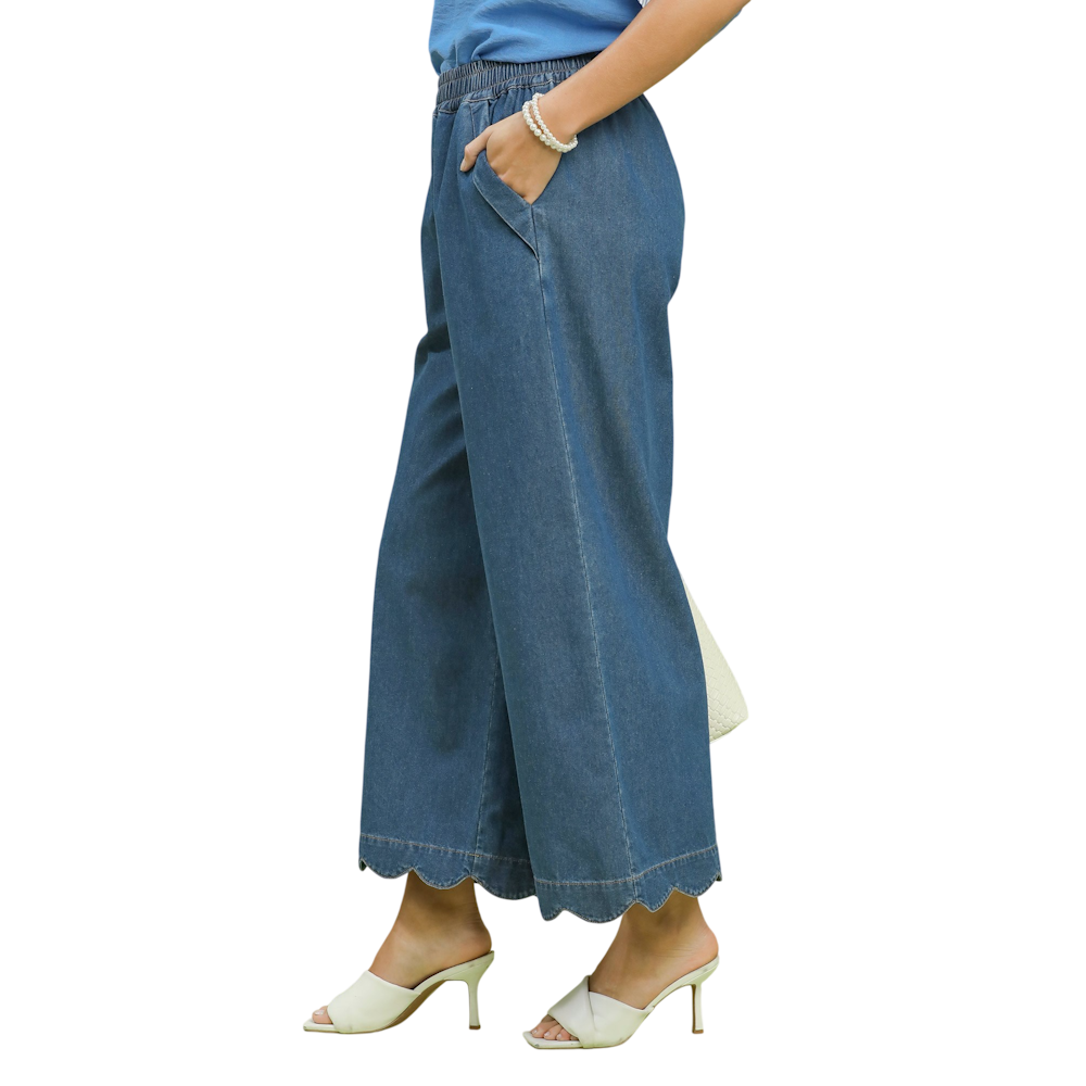 Side profile of a person wearing wide-leg denim pants with a scalloped hem and white heeled sandals.