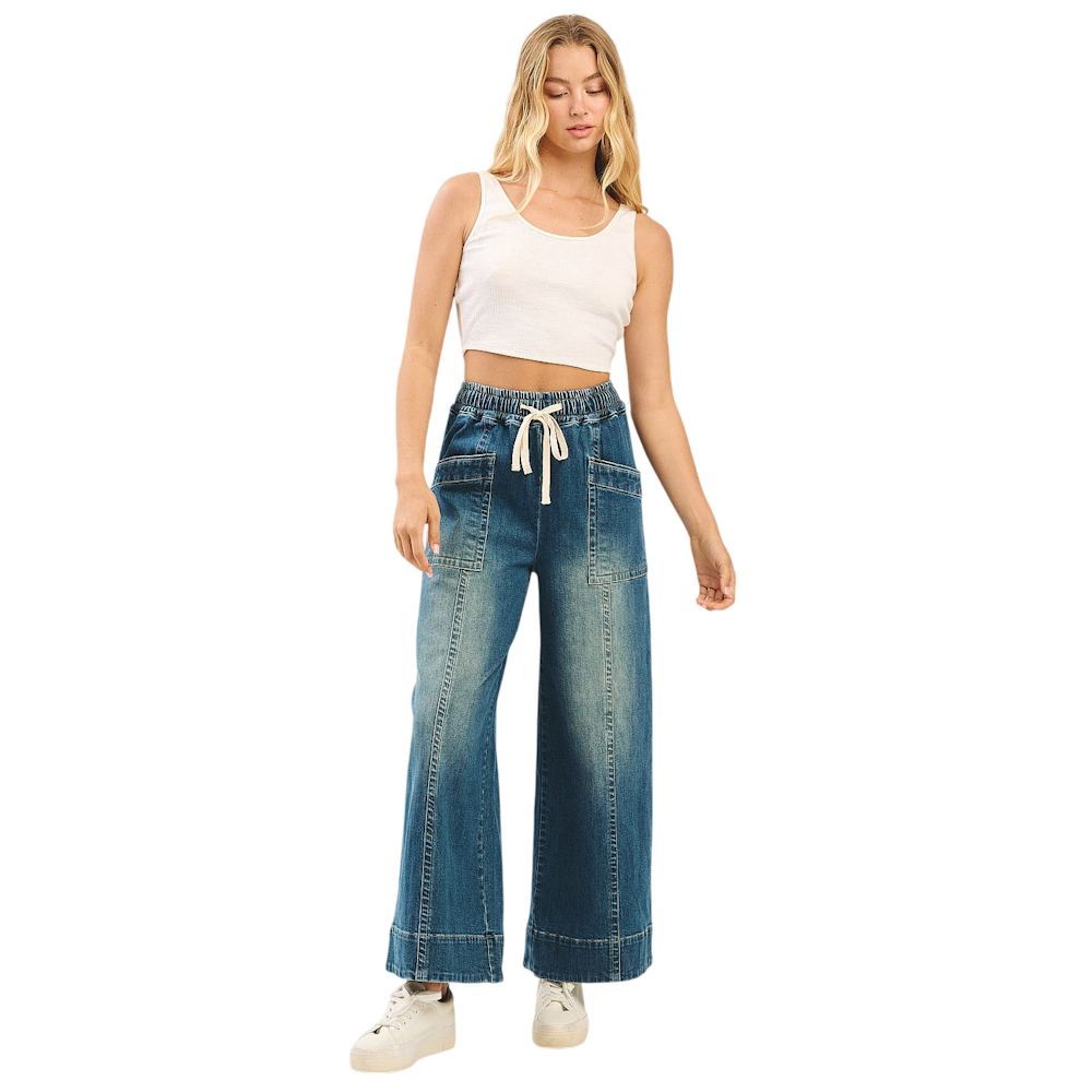 Model wearing faded wide-leg denim pants with elastic drawstring waist and oversized front pockets.