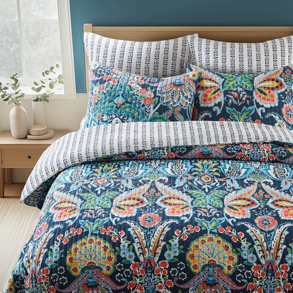 Bed styled with a vibrant blue, orange, and yellow botanical quilt, matching shams, and stripe accent pillows.