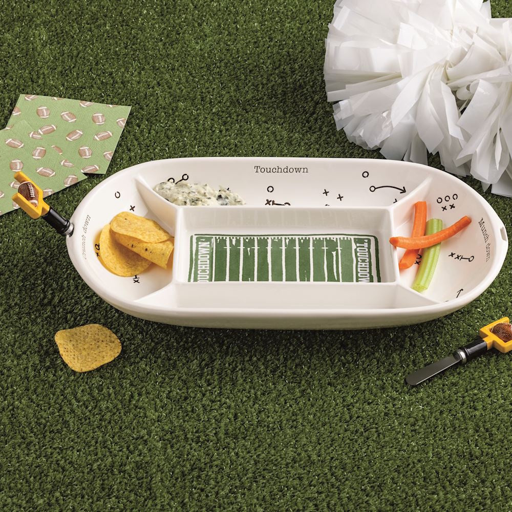 Divided football field serving platter filled with snacks on green turf with pom-poms.