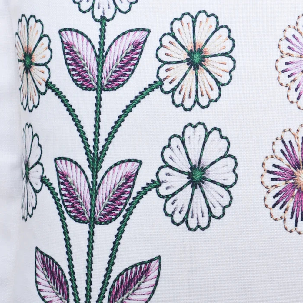 Close-up of white floral embroidery on a pillow with green stems, purple accented leaves, and scalloped flower petals.