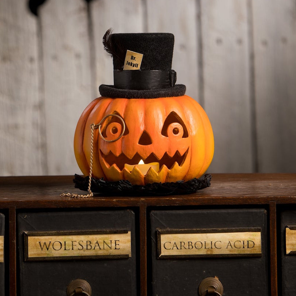 Illuminated Dr. Jekyll pumpkin lantern wearing a black top hat and monocle, sitting on wooden drawers.