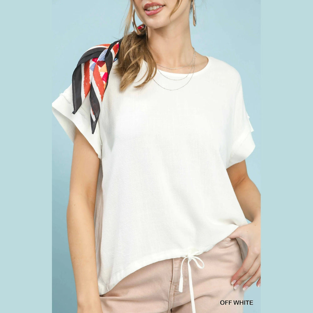 Woman in an off-white drawstring linen-blend top with short sleeves and a scarf accent, against a light blue background.