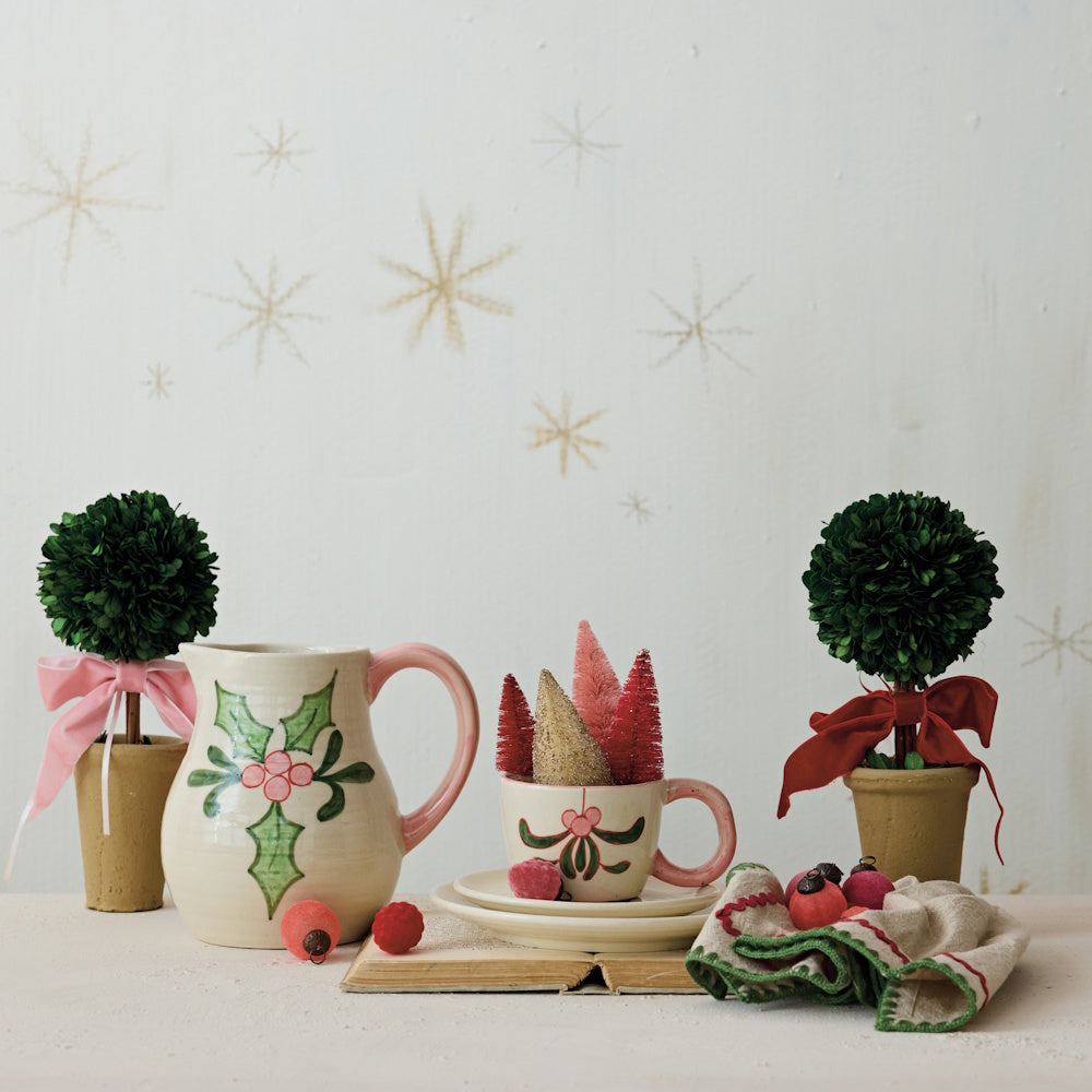 Small preserved boxwood topiary trees in pots with ribbons set among festive holiday decor.