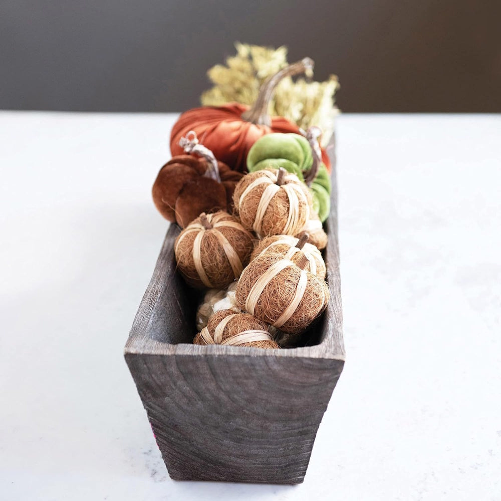 Wooden trough dough bowl filled with natural coco fiber, raffia, and velvet decorative pumpkins.
