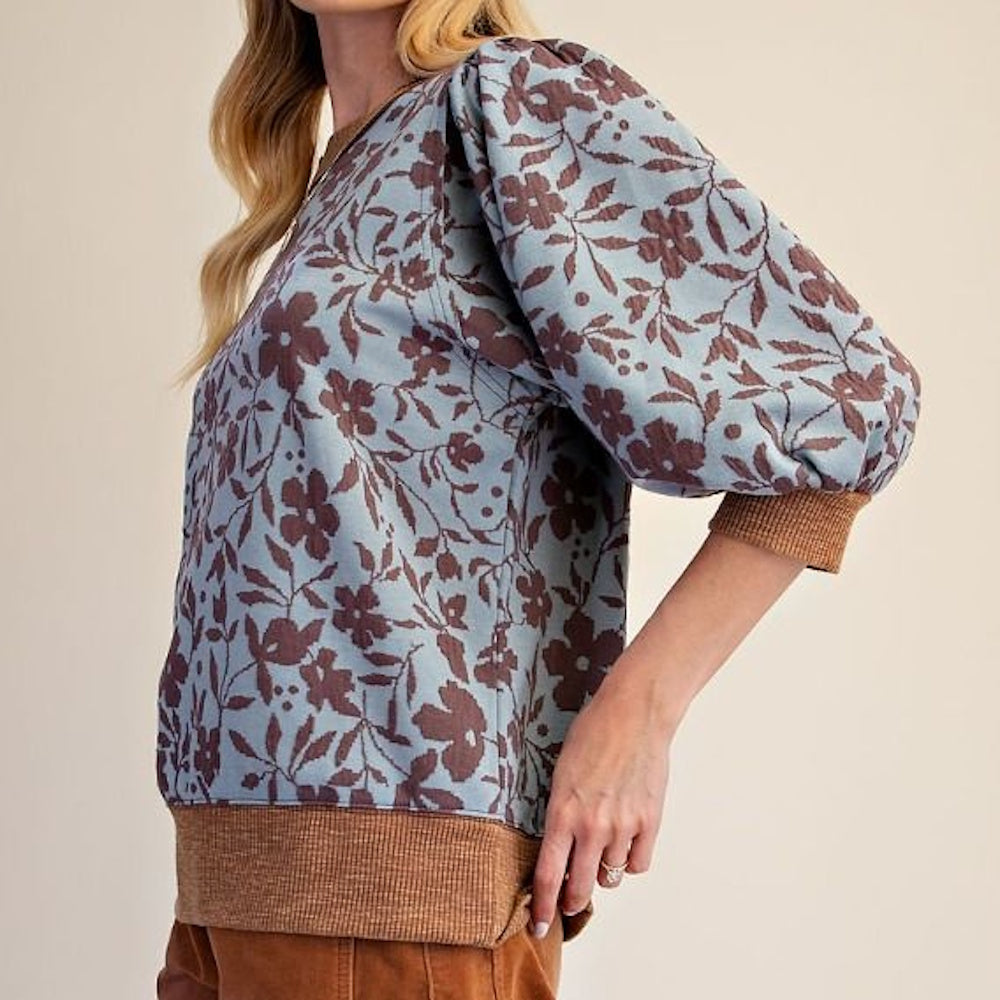 Side view of dusty blue floral knit top with brown ribbed cuffs and hem.