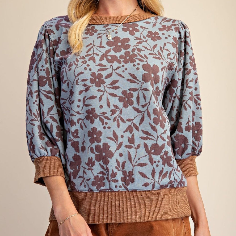 Dusty blue top with brown floral pattern, ribbed neckline, three-quarter sleeves, and banded hem.