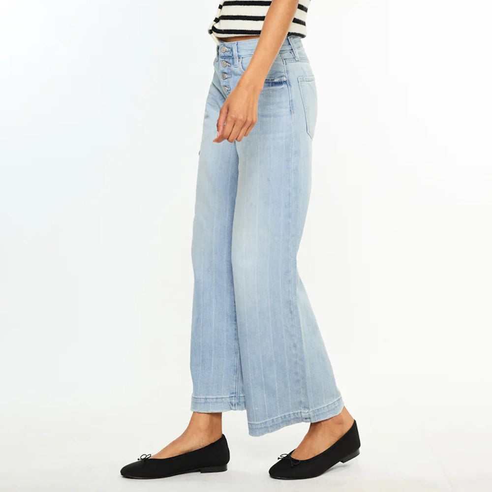 Woman wearing light wash 90s wide-leg jeans with button fly and black ballet flats, side view on white background.