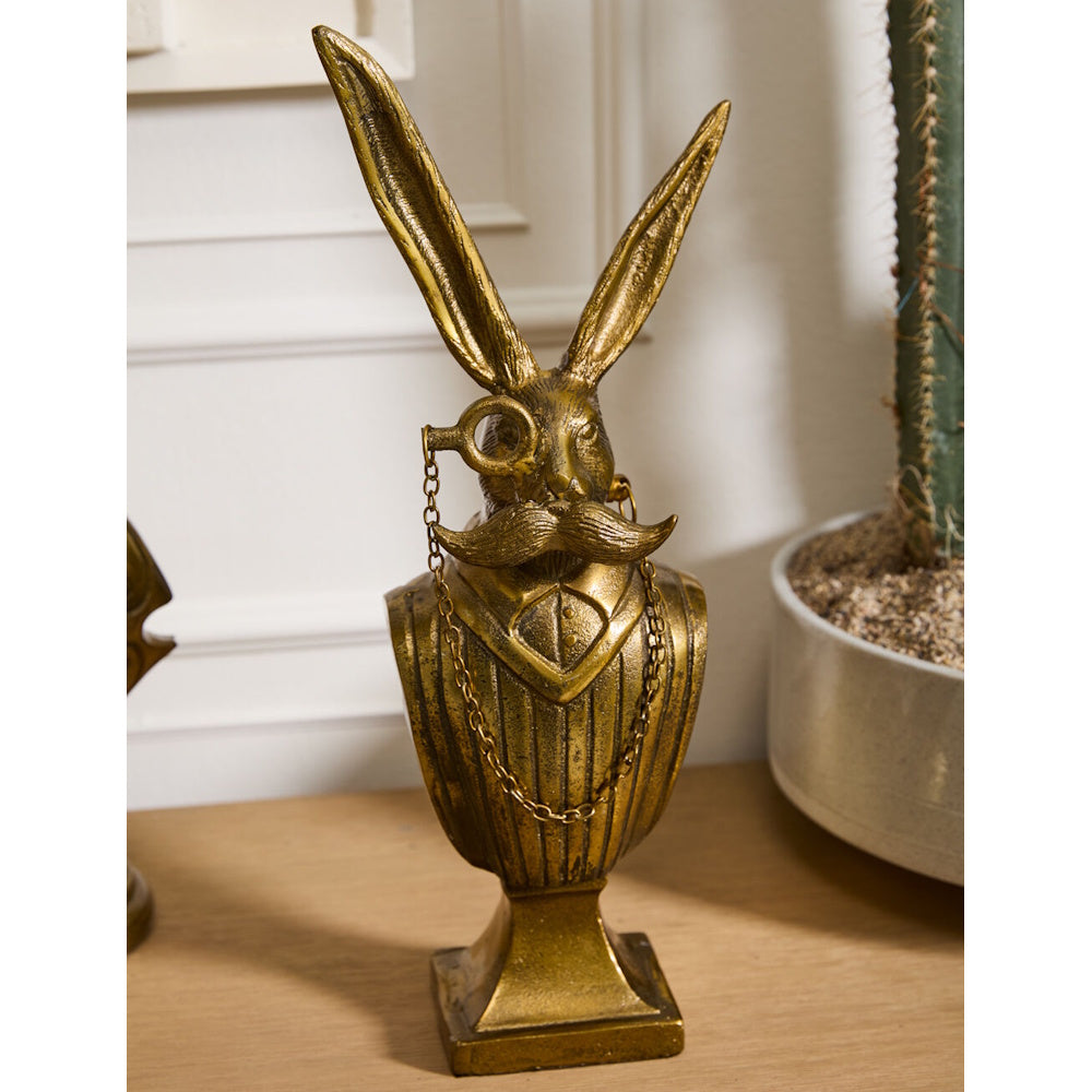 Front view of the antique gold rabbit bust displayed on a wooden surface beside a potted cactus.