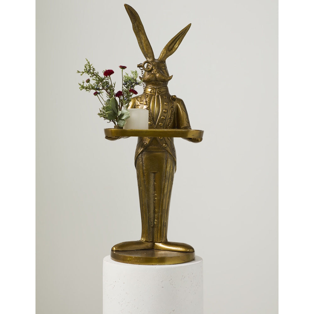 Gold rabbit butler statue with a monocle holding a tray with a candle and small flower bouquet.
