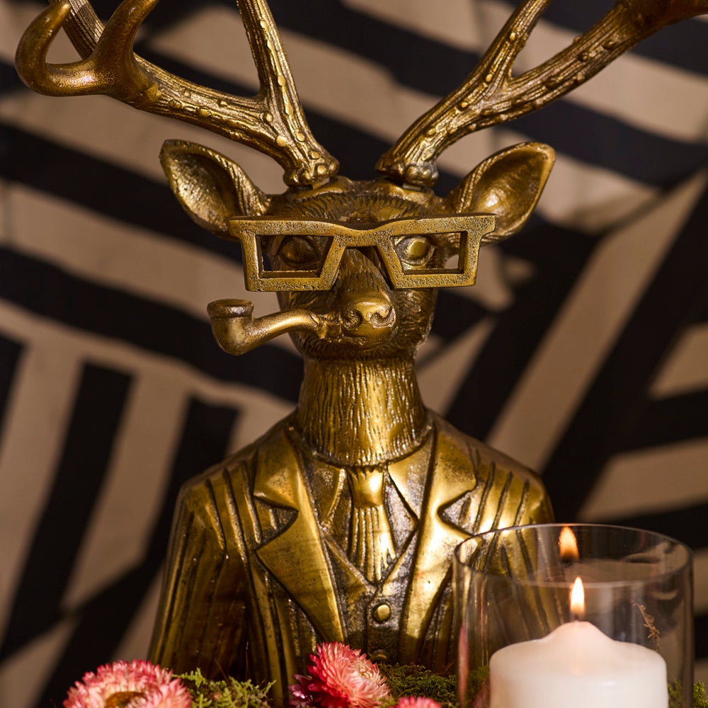 Golden deer statue wearing a suit and glasses, smoking a pipe beside a lit candle.