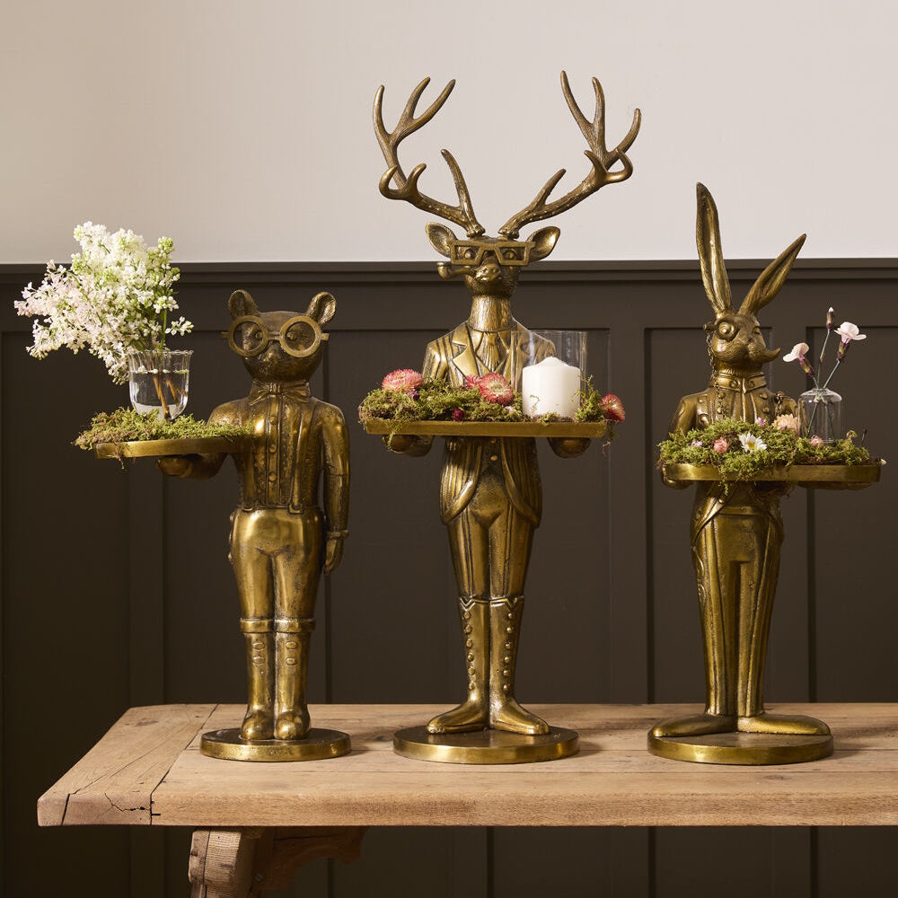 Three brass animal waiter statues holding trays decorated with flowers and a candle.