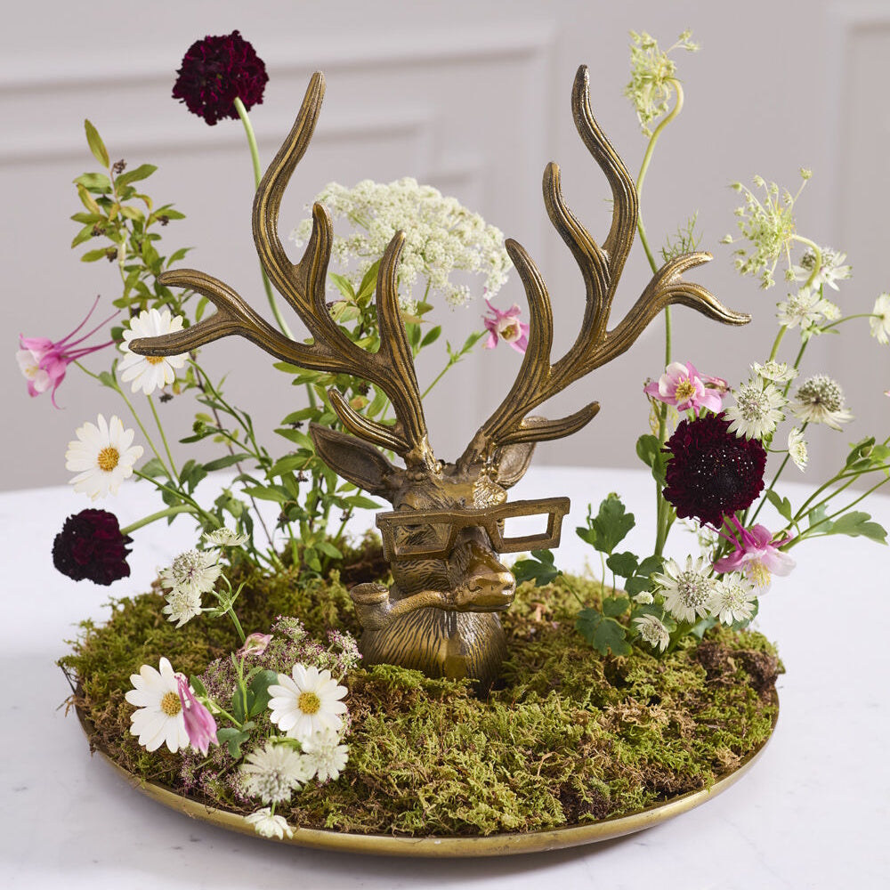 Bronze deer tray with glasses and a pipe, styled with a moss base and assorted wildflowers.