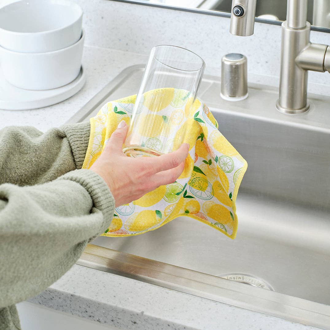 Person cleaning a glass with a yellow cloth in a kitchen sink.