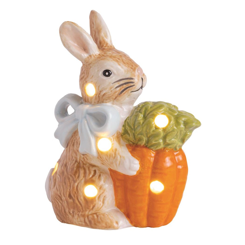 Ceramic light-up Easter bunny figurine holding a large carrot with a blue bow, decorative spring holiday shelf sitter.