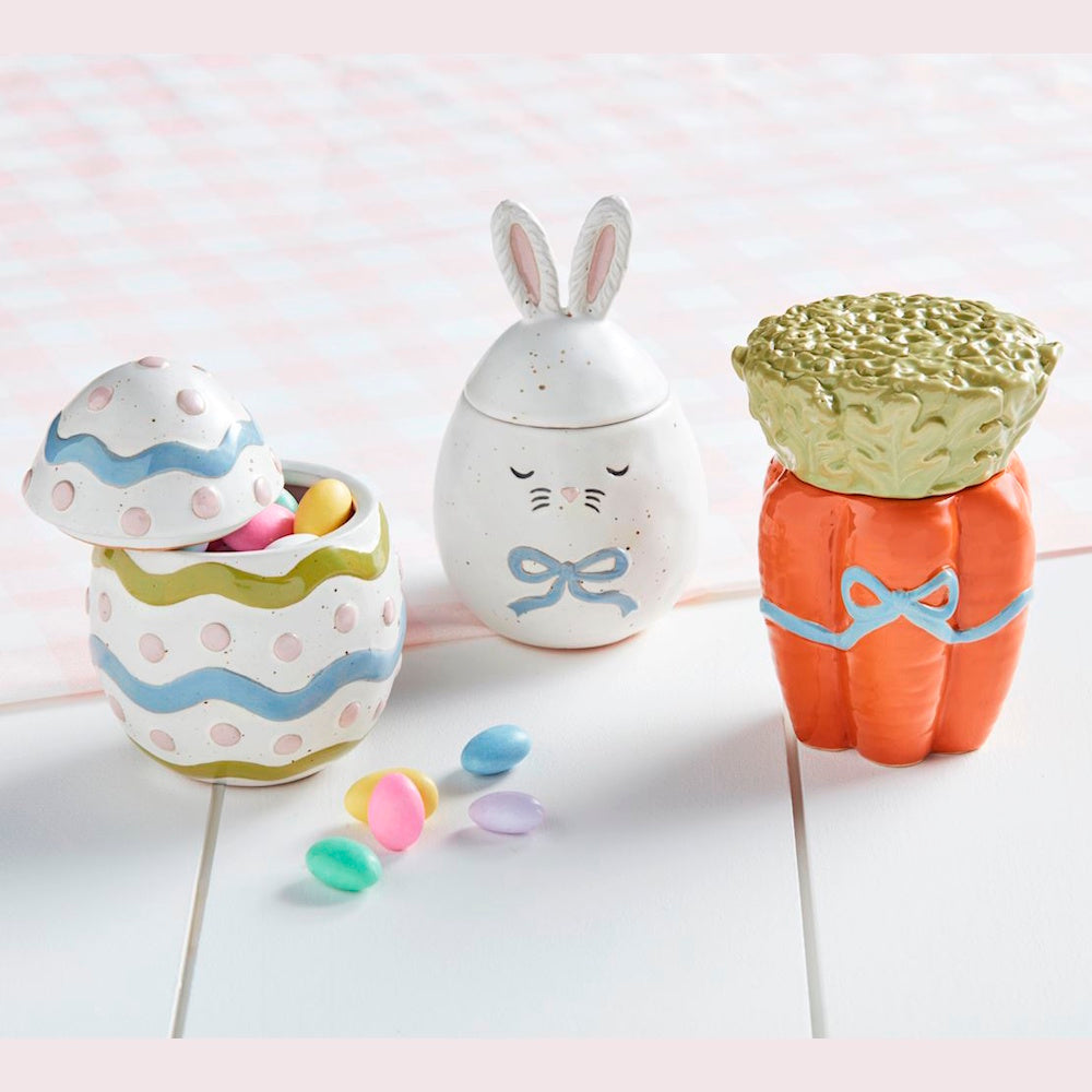 Three small Easter-themed ceramic jars shaped like a decorated egg, a white bunny, and an orange carrot.