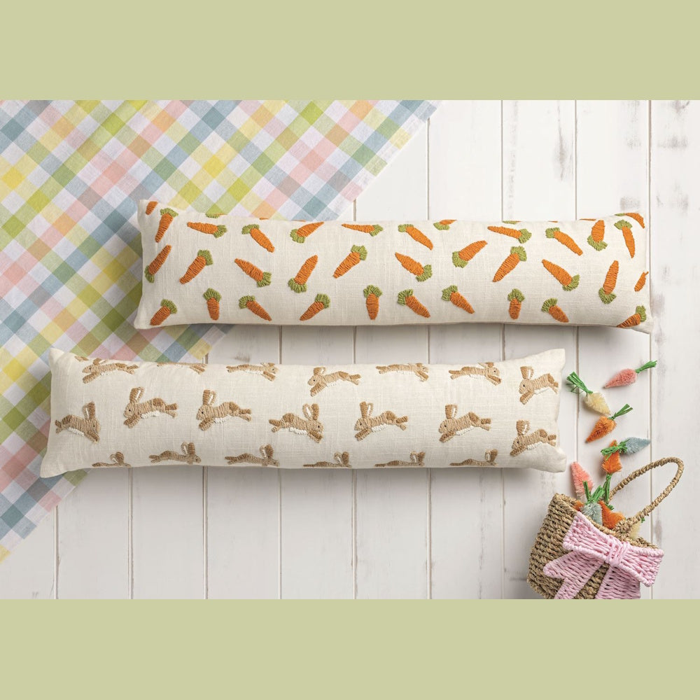 Embroidered Easter lumbar pillows with bunny and carrot patterns on white wood background with spring decor.