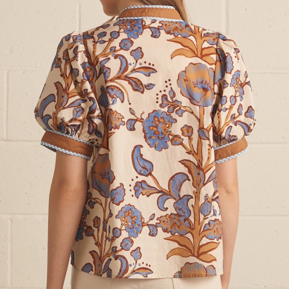 Back view of an ecru top featuring blue floral print, brown sleeve cuffs, and checkered trim.