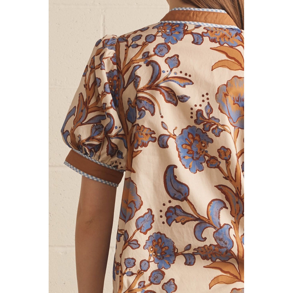 Close-up back view of an ecru floral print top showing puff sleeve detail and blue-checked trim.