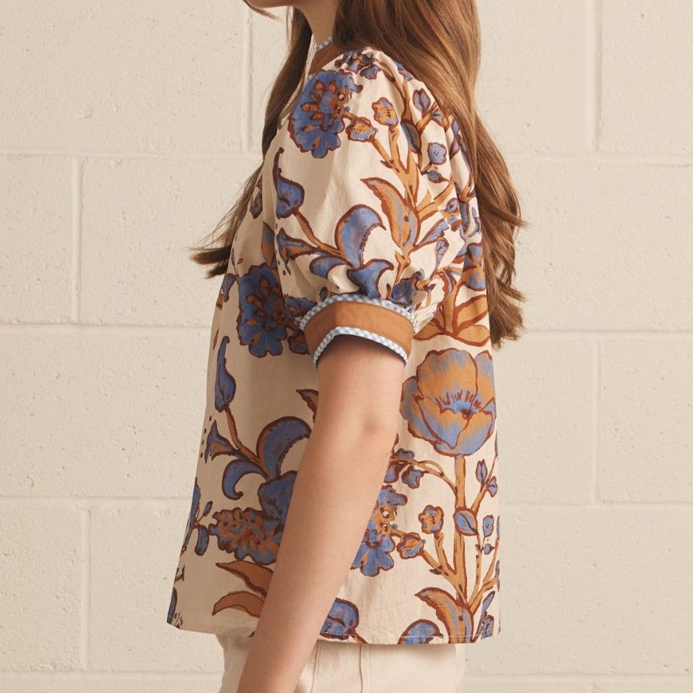 Side profile of an ecru floral top featuring blue botanical prints and brown cuffed puff sleeves.