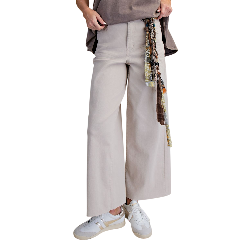 Front view of high-waisted ecru wide-leg twill pants styled with a patterned belt sash and sneakers.