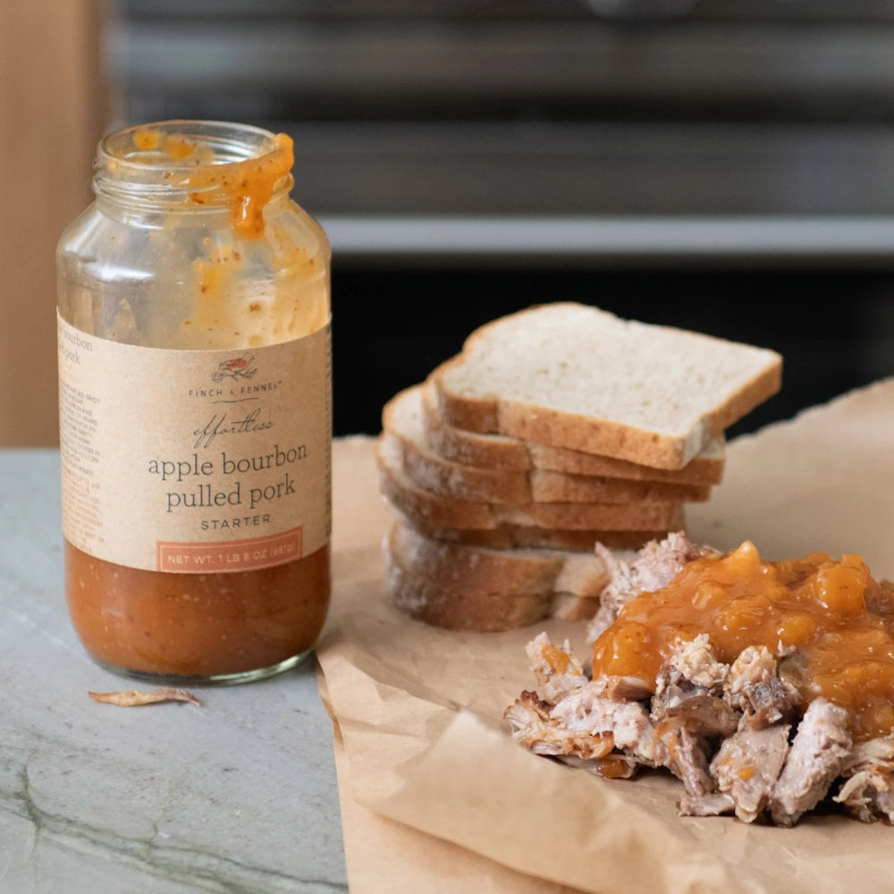 Apple bourbon pulled pork on parchment paper with bread slices and a jar of Finch + Fennel pork starter sauce.