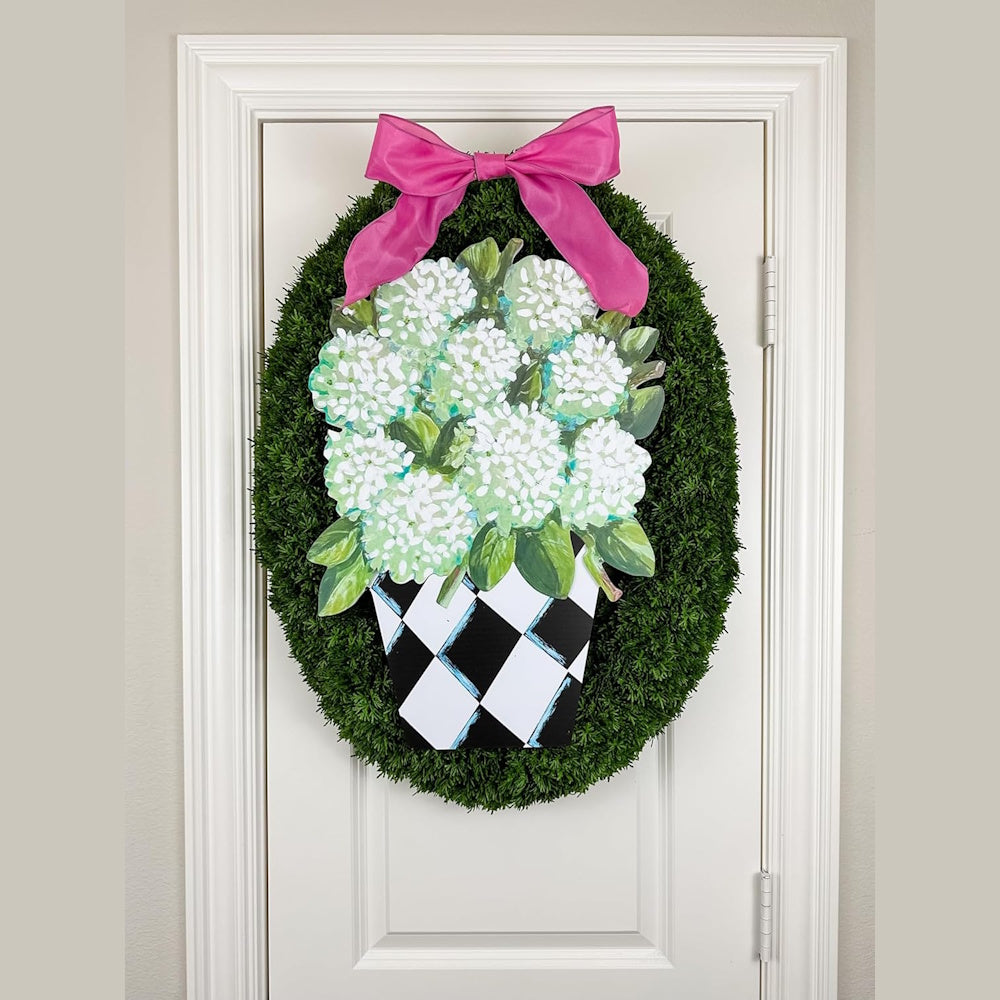 Hydrangea door hanger with a pink bow and checkered pot on a green boxwood wreath, hanging on a white door.