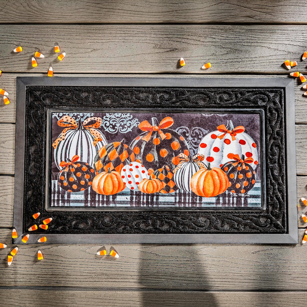 Halloween doormat with elegant patterned pumpkins and orange bows on a dark background, scattered candy corn.