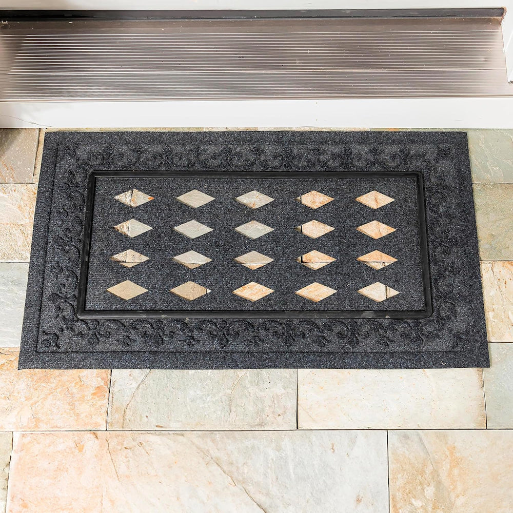 Black fleur-de-lis embossed doormat tray with a diamond pattern insert on a stone tile entryway.