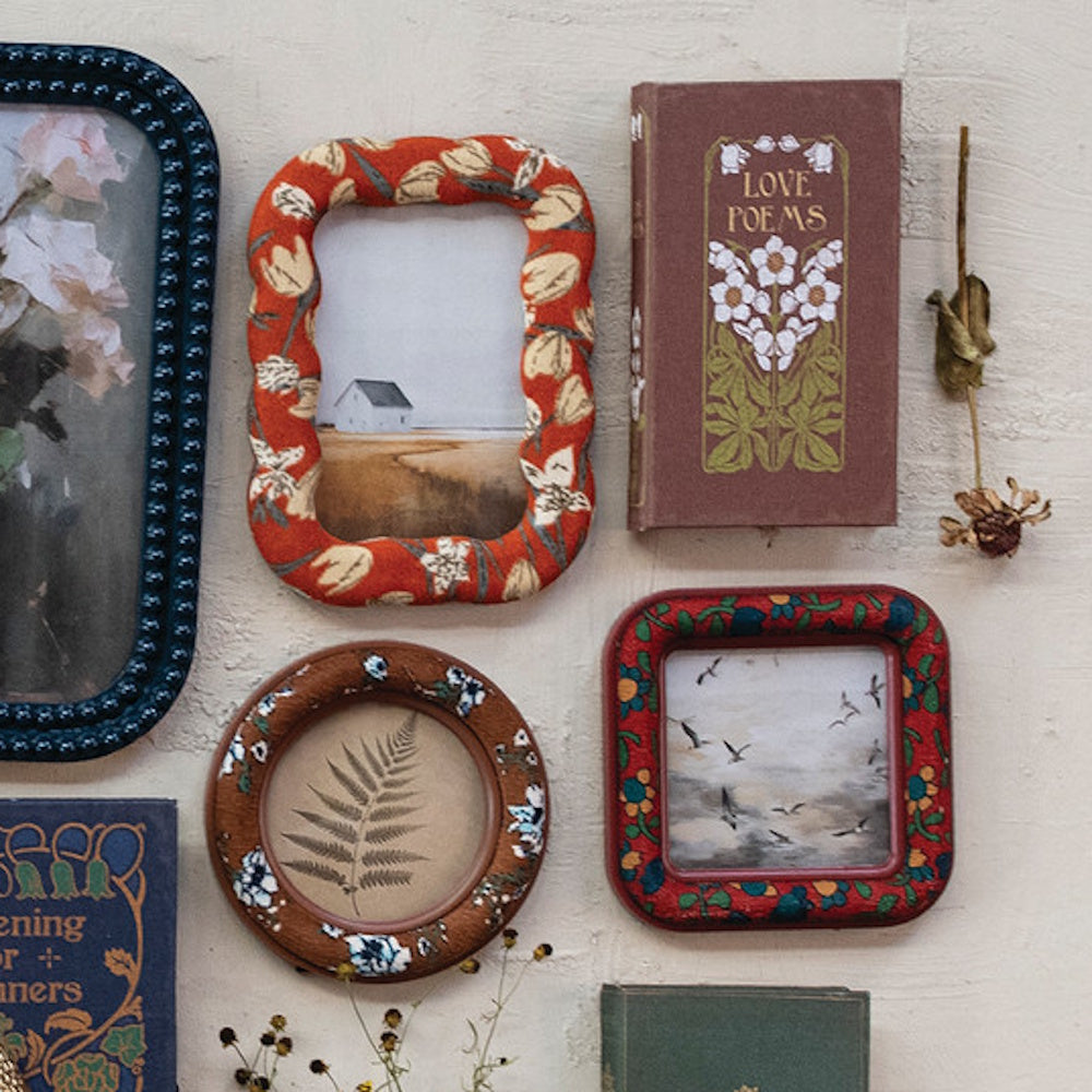Wall gallery with floral fabric picture frames, vintage books, a pressed fern, and dried flowers.