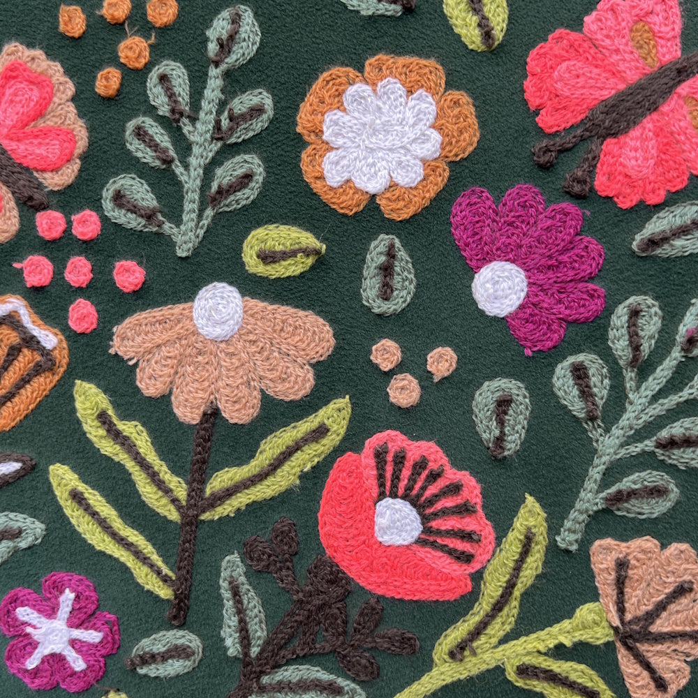 Hand-embroidered floral pattern with colorful textured flowers and leaves on dark green fabric.