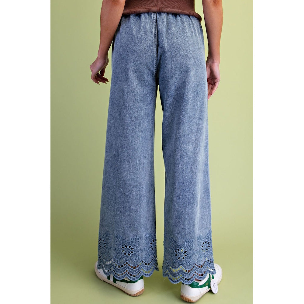Back view of wide-leg light wash jeans featuring scalloped eyelet embroidery along the bottom hem.
