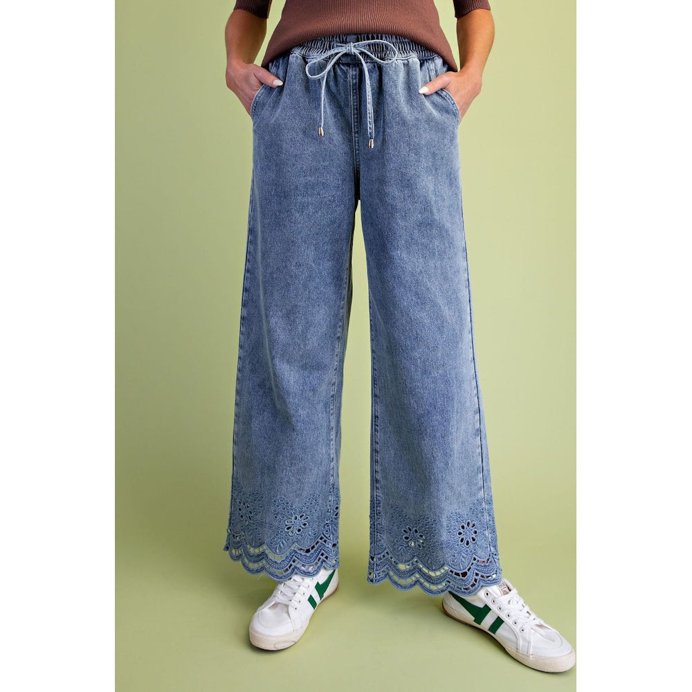 Wide-leg drawstring denim pants featuring embroidered eyelet scalloped hems, paired with sneakers.
