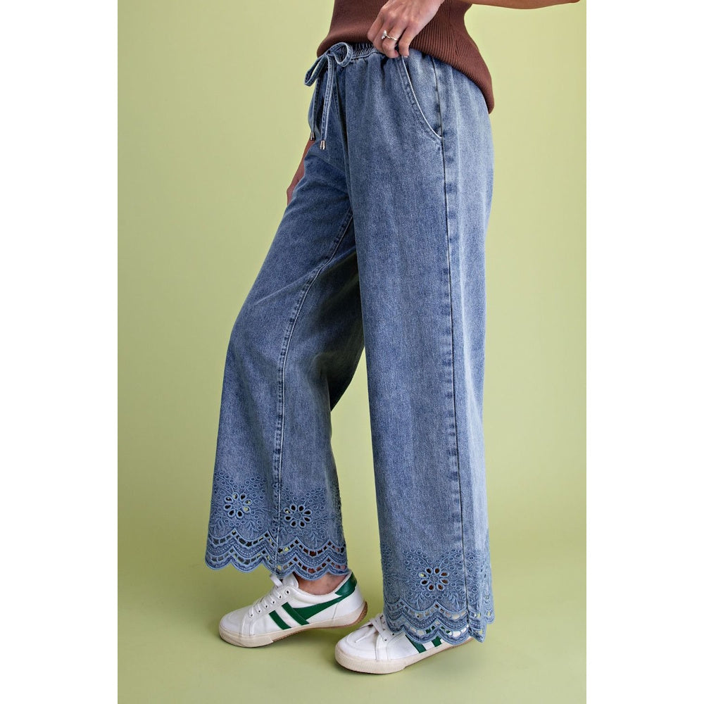 Side view of washed blue denim wide-leg pants featuring a drawstring waist and eyelet lace hems.