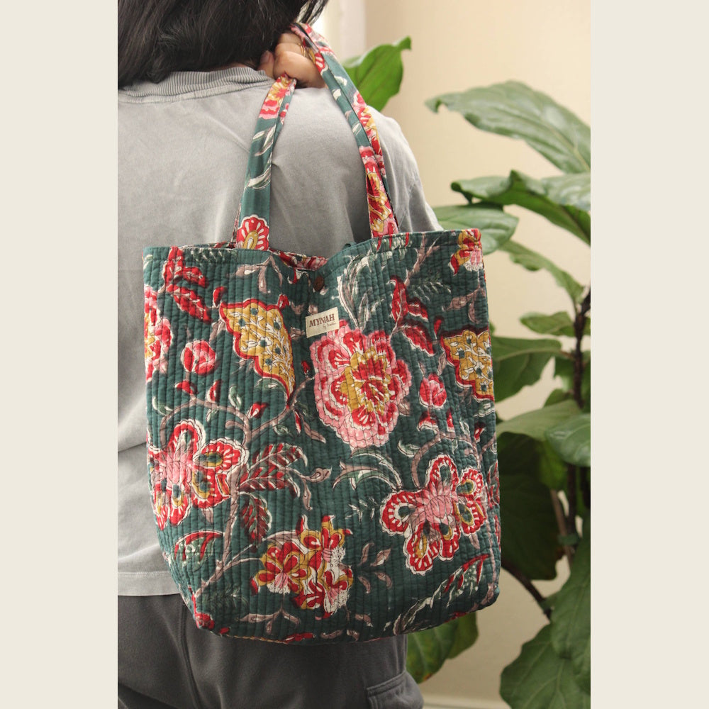 Emerald Forest Floral Quilted Reversible Tote Bag by MYNAH over a person's shoulder in front of a fiddle-leaf fig.