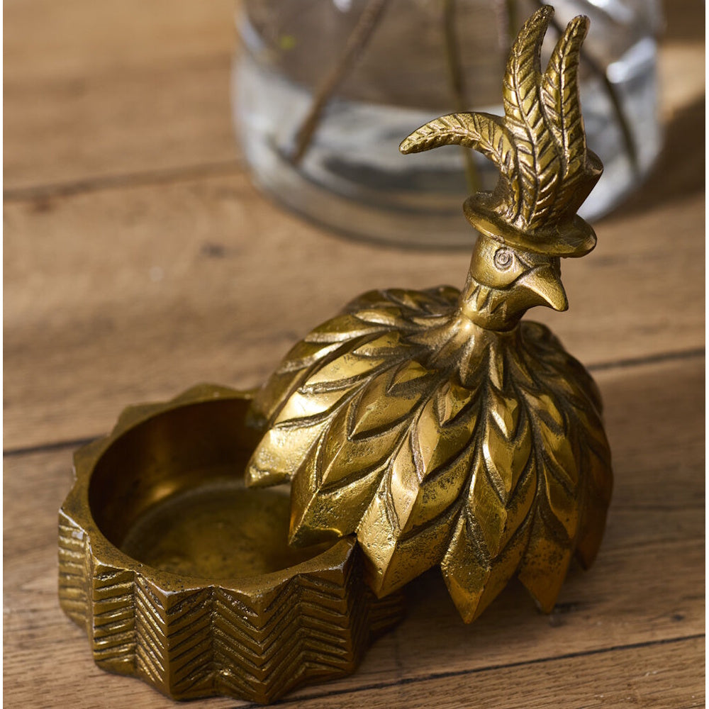 Person holding open the lid of an antique gold decorative box shaped like a bell with a feathered bird top hat handle.
