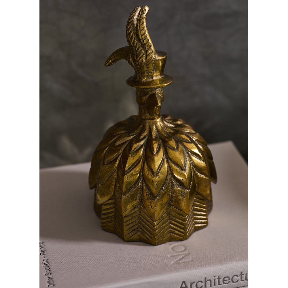 Antique gold decorative box shaped like a bell with a feathered bird top hat handle, displayed on top of a book.