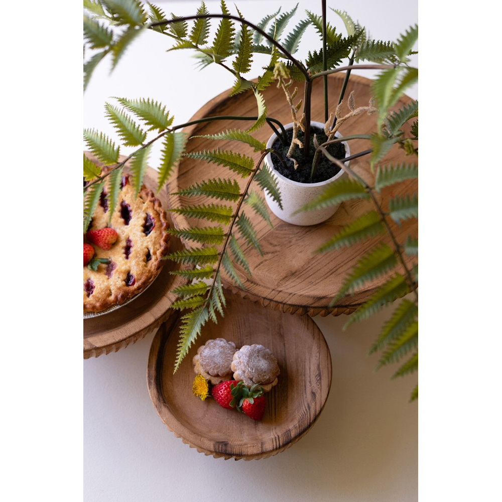Top-down view of three etched wooden pedestals displaying pastries, a pie, and a potted plant.
