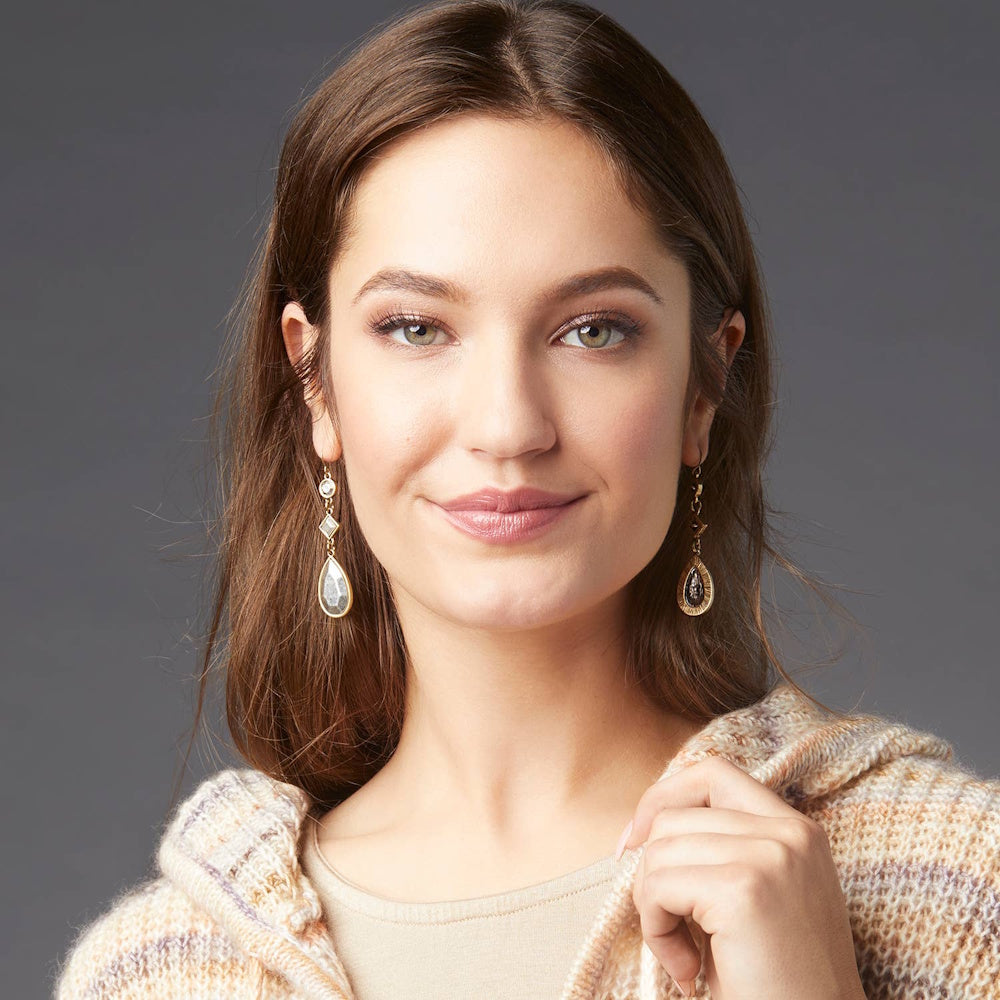Woman wearing geometric faceted silver teardrop dangle earrings with gold accents.