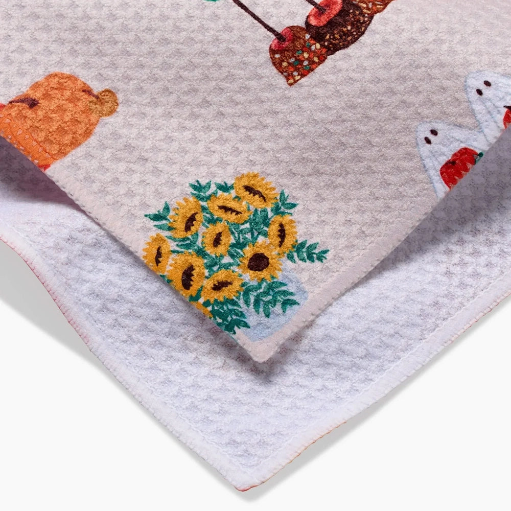 Close-up of a white waffle-weave towel featuring autumn illustrations including sunflowers and candy apples.