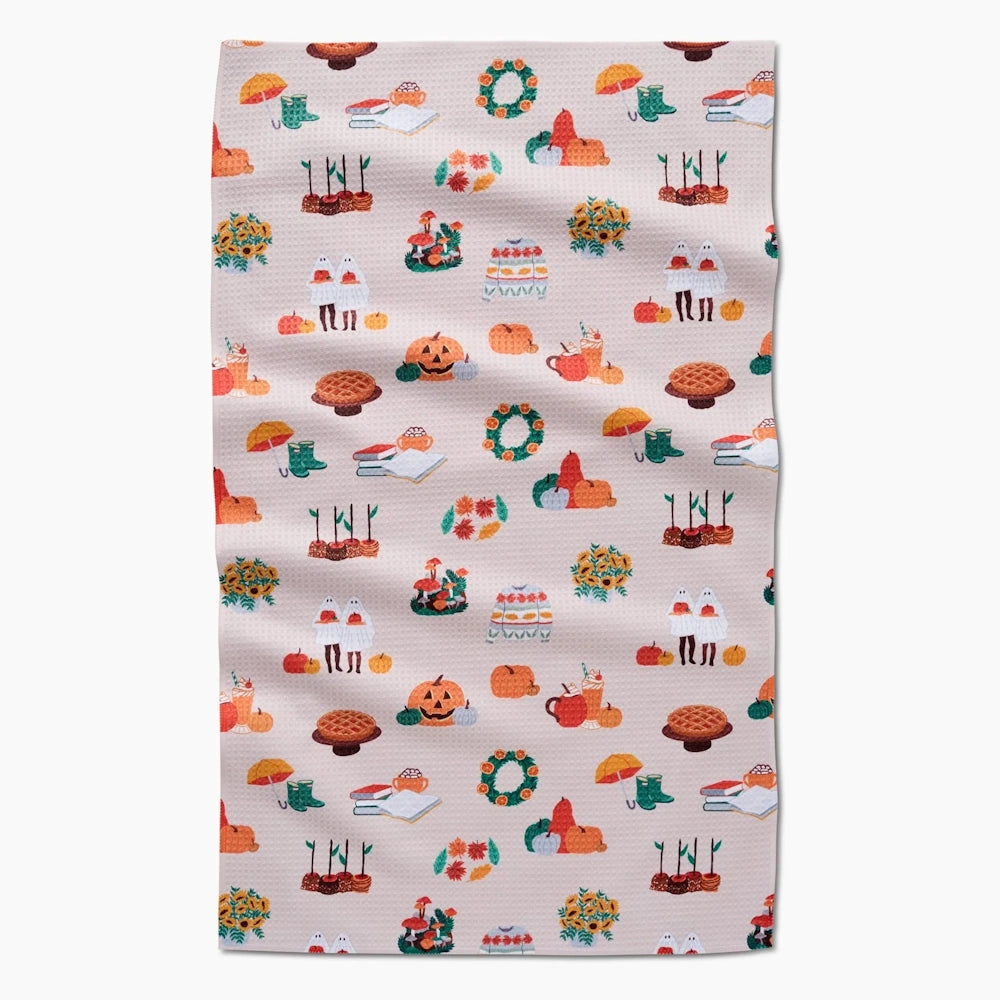 A light pink waffle-weave kitchen towel featuring a repeating pattern of small autumn-themed illustrations.