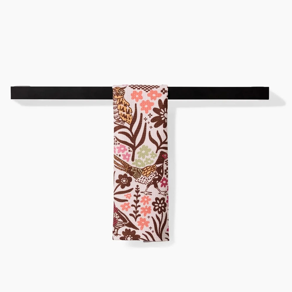 White bar towel with a colorful pattern of birds and flowers hanging from a sleek black towel bar.