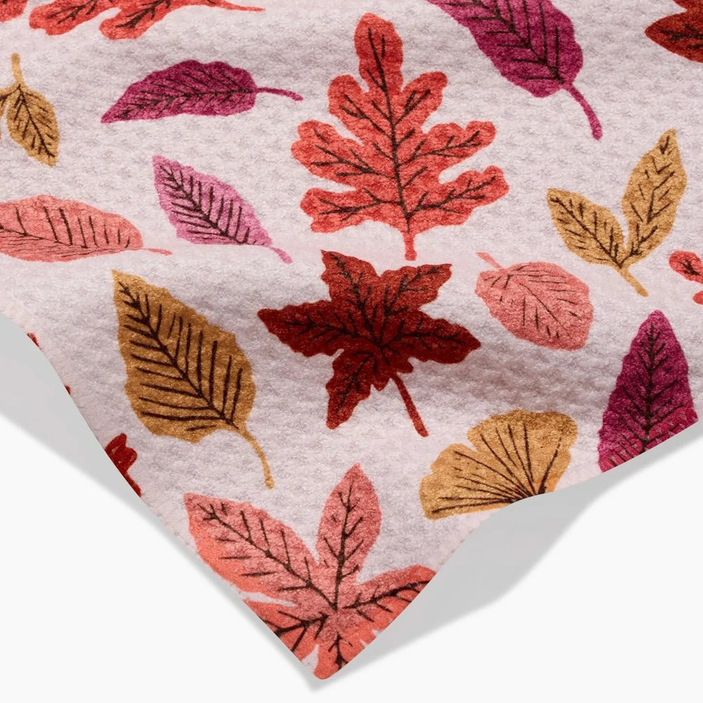 Close-up of a white textured fabric towel featuring a colorful pattern of scattered autumn leaves.