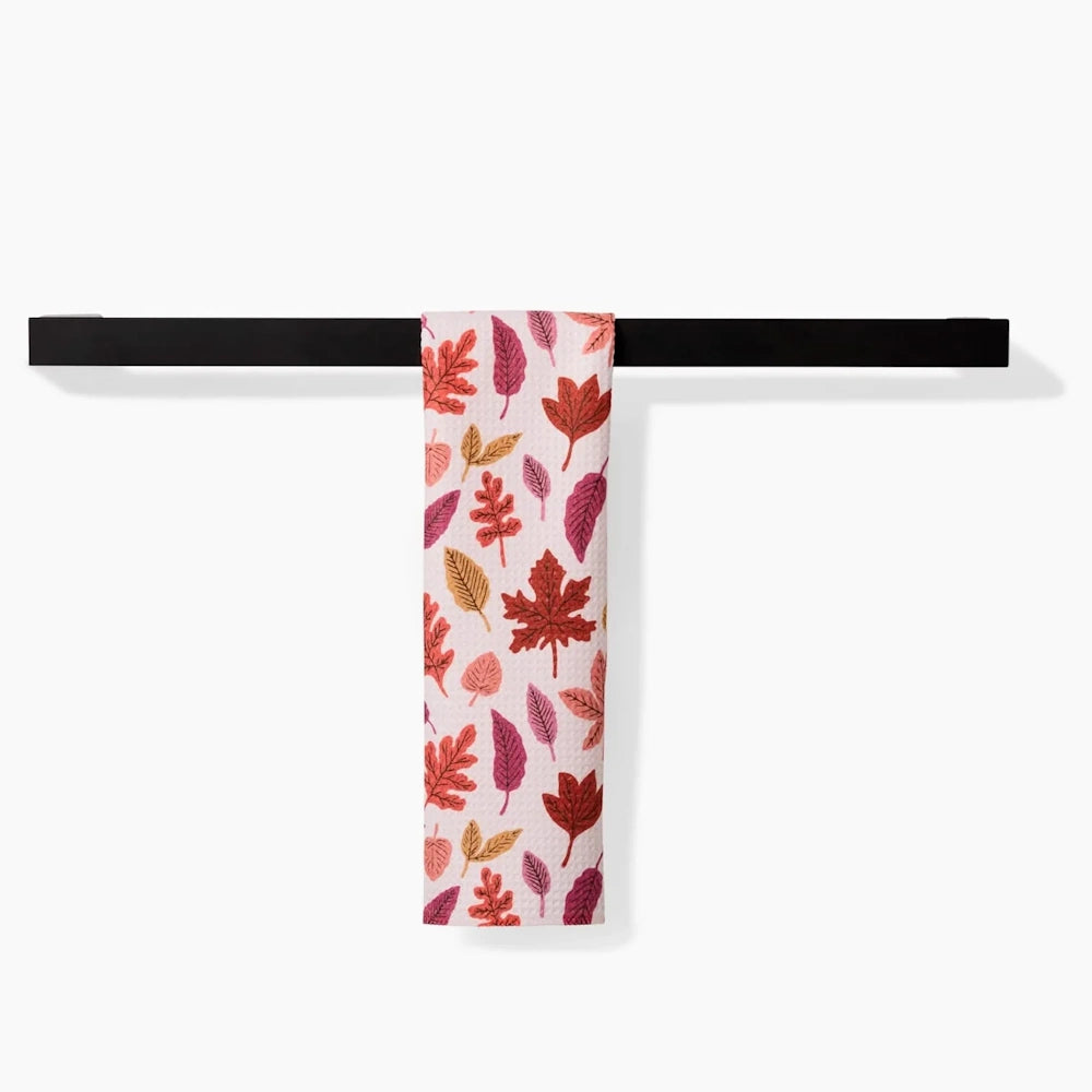 White kitchen towel with an autumn leaves pattern hanging over a sleek black bar.