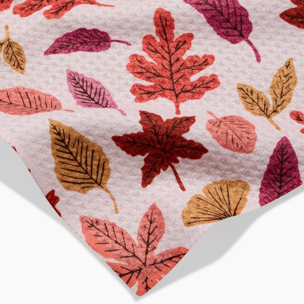 Close-up of a light pink fabric patterned with various autumn leaves in shades of orange, magenta, and gold.