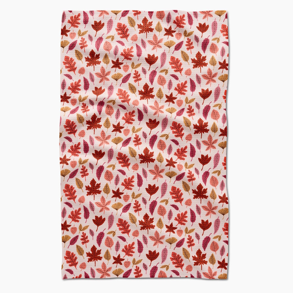 A flat-lay view of a light-colored kitchen towel patterned with various colorful fall leaves.