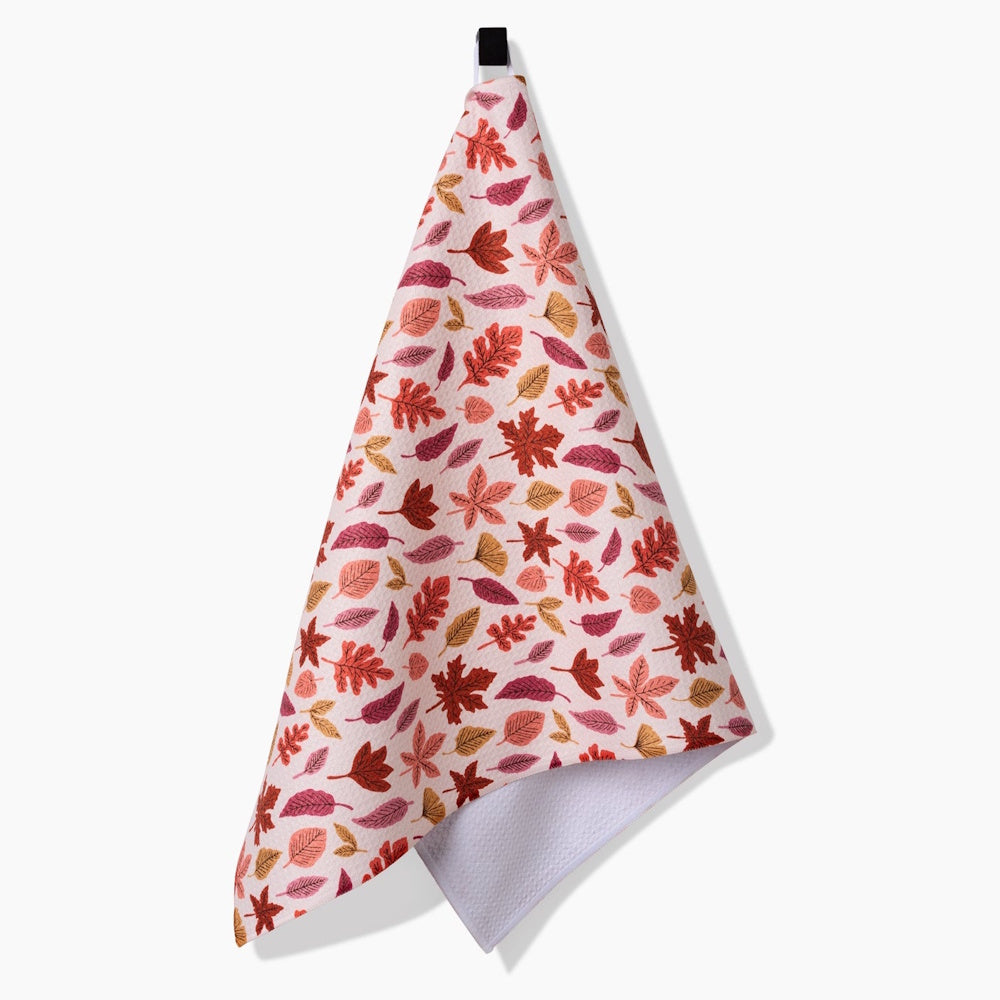 A hanging tea towel with a colorful autumn leaf pattern in shades of red, orange, pink, and brown.