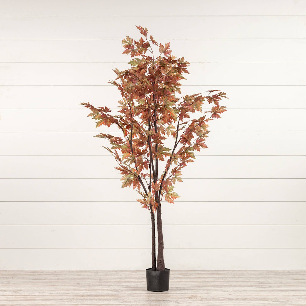Artificial fall maple tree with orange and green leaves in a small black pot against a white panel wall.