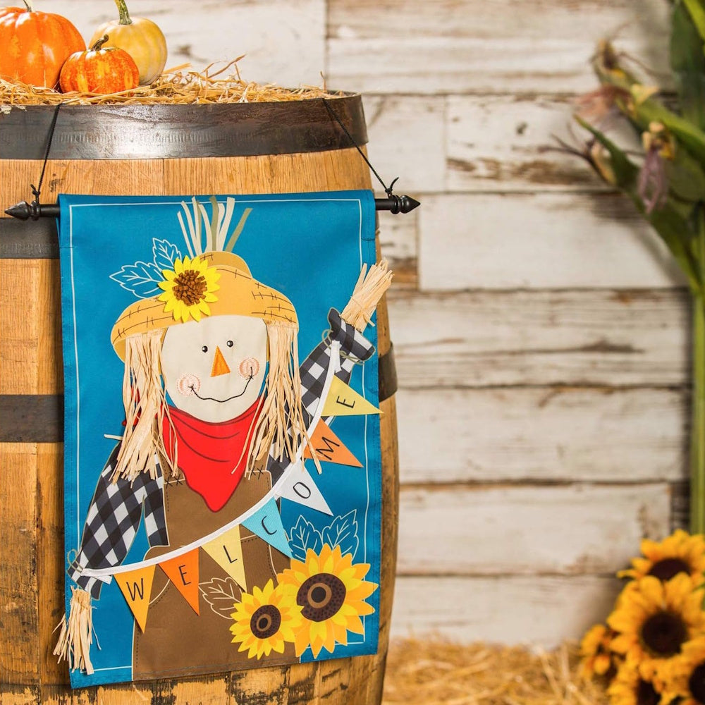 Blue fall decorative flag featuring a smiling scarecrow with a "WELCOME" banner hanging on a wooden barrel.